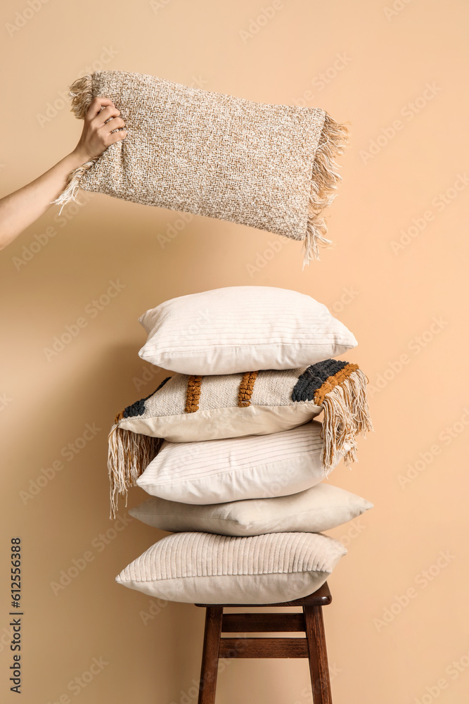 Woman taking pillow from stool near beige wall