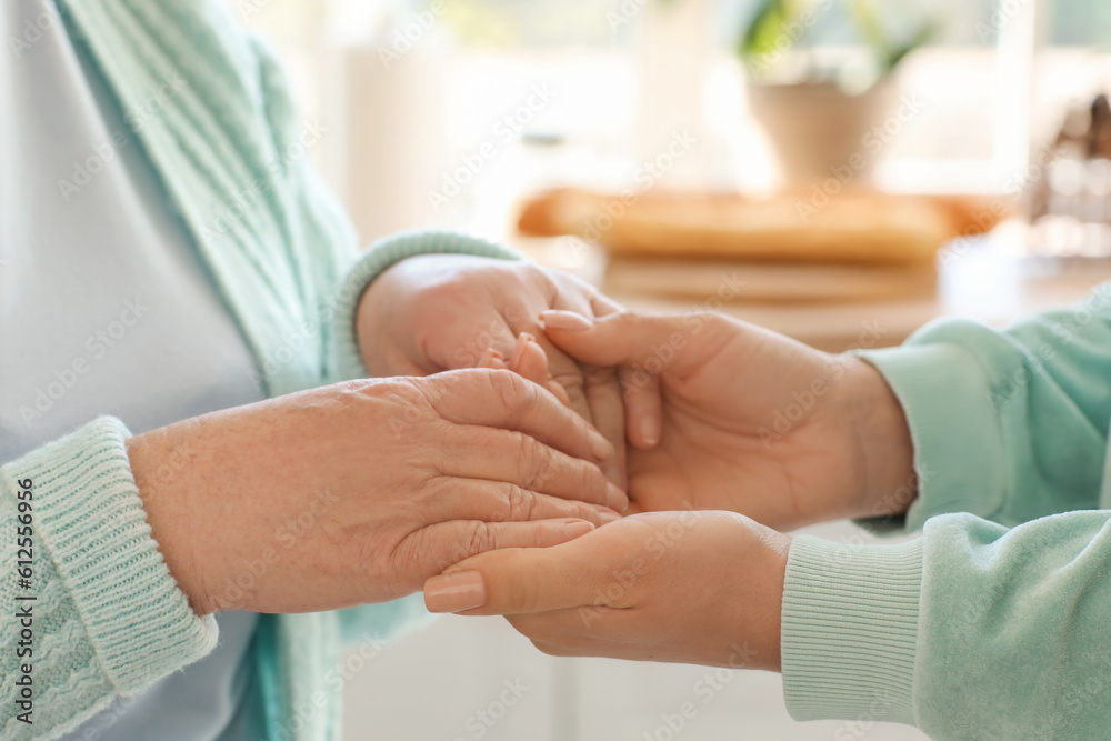 Senior woman with her granddaughter holding hands at home, closeup