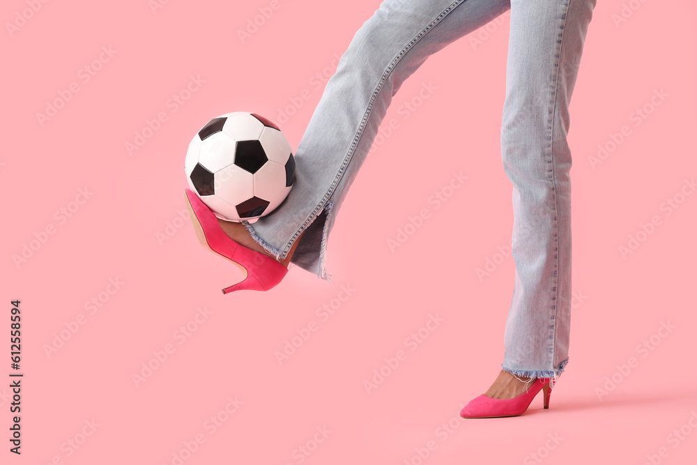 Legs of young woman wearing high heels and playing with soccer ball on pink background