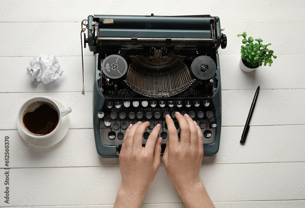 Woman typing on typewriter with cup of coffee, crumpled paper and houseplant on white wooden backgro