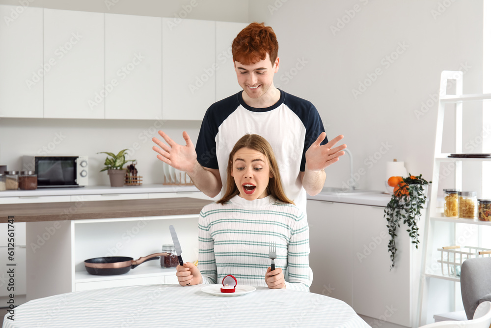 Young man proposing to his happy girlfriend in kitchen