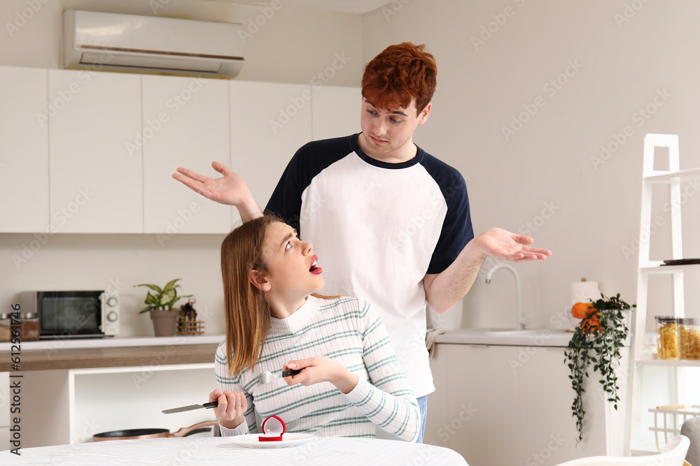 Young man proposing to his displeased girlfriend in kitchen