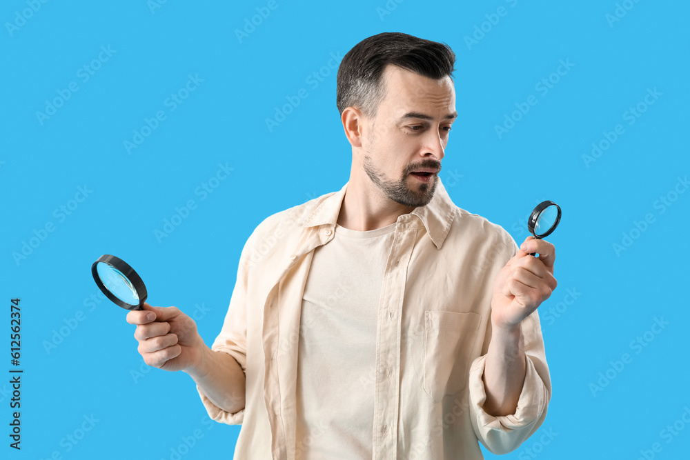 Handsome man with magnifiers on blue background