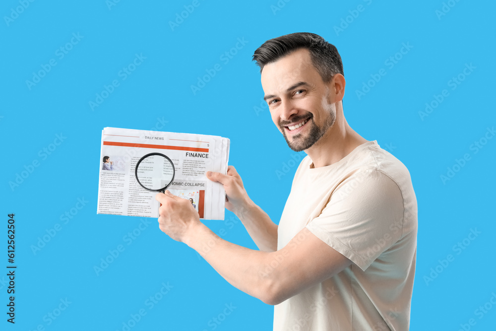 Handsome man with magnifier and newspaper on blue background