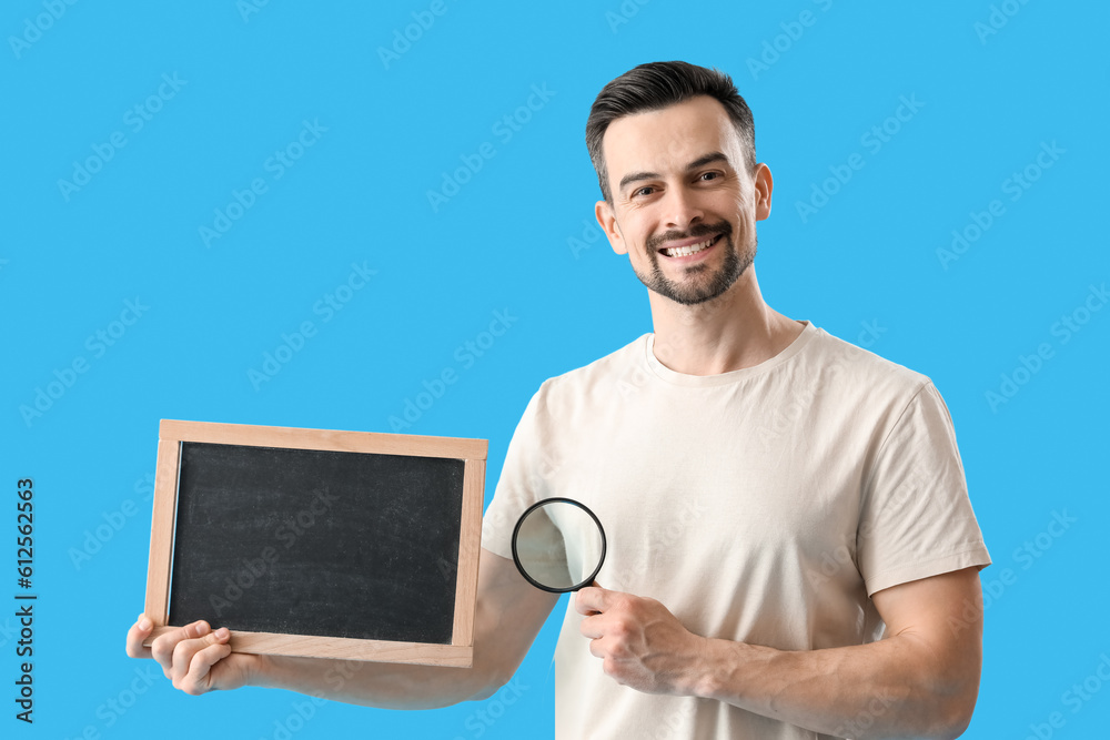 Handsome man with magnifier and chalkboard on blue background