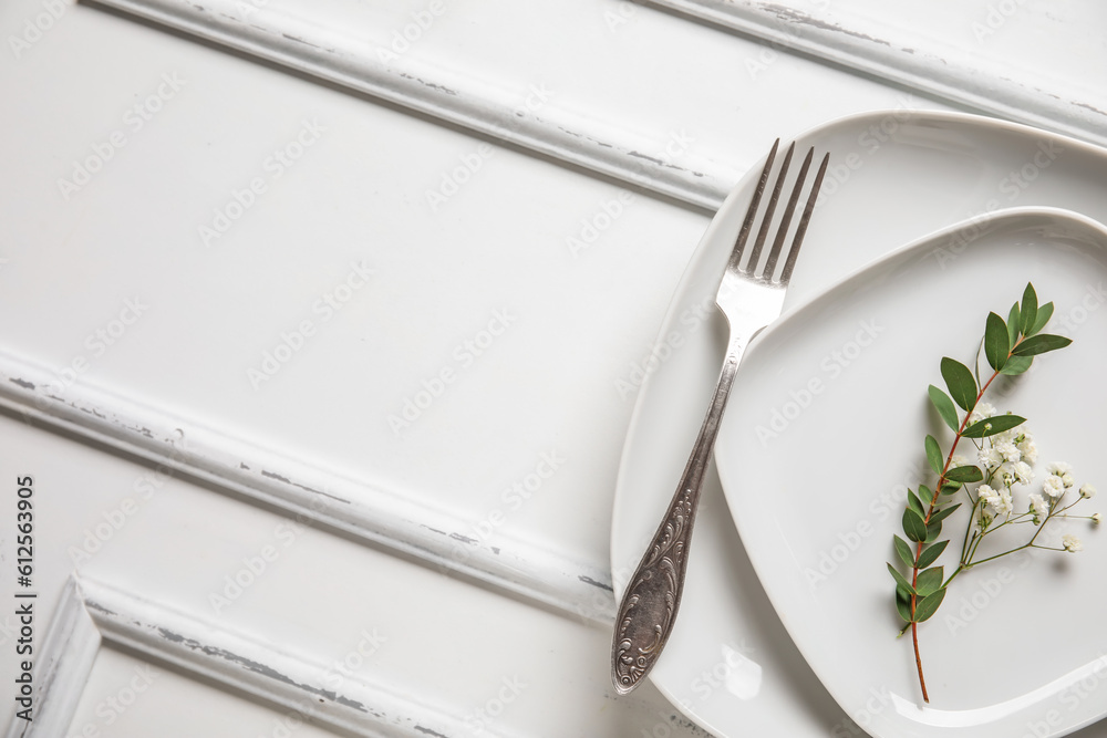 Plates with silver cutlery and flowers on white wooden background