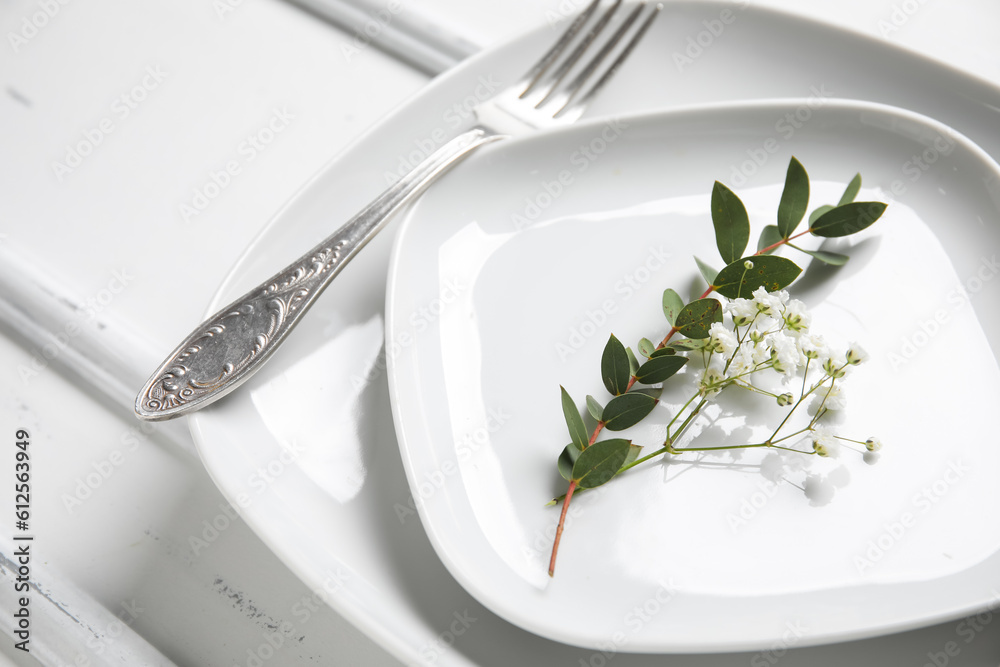 Plates with silver cutlery and flowers on white wooden background