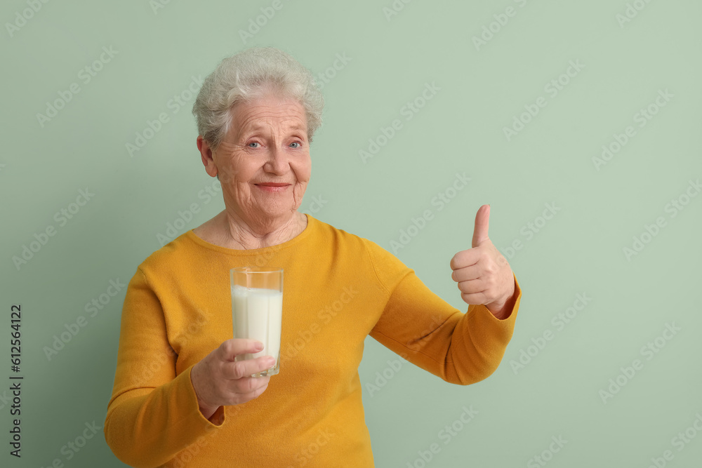 Senior woman with glass of milk showing thumb-up on green background