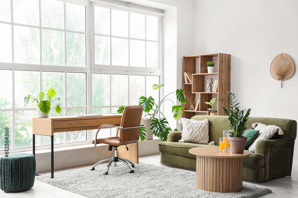 Interior of stylish living room with cozy green sofa and comfortable workplace near big window