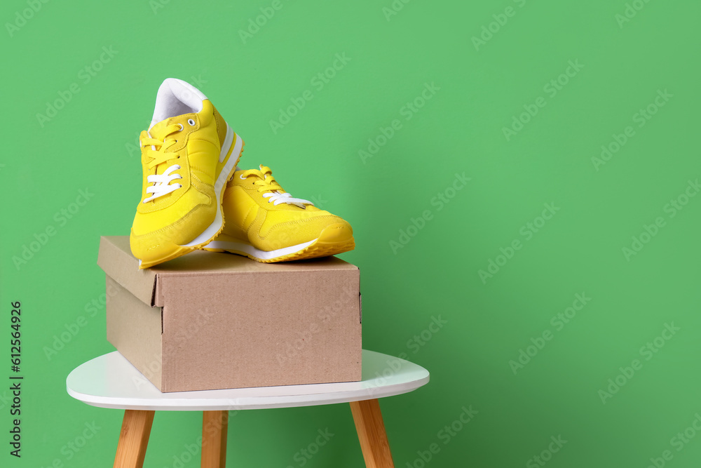 Table with cardboard box and stylish sneakers on green background