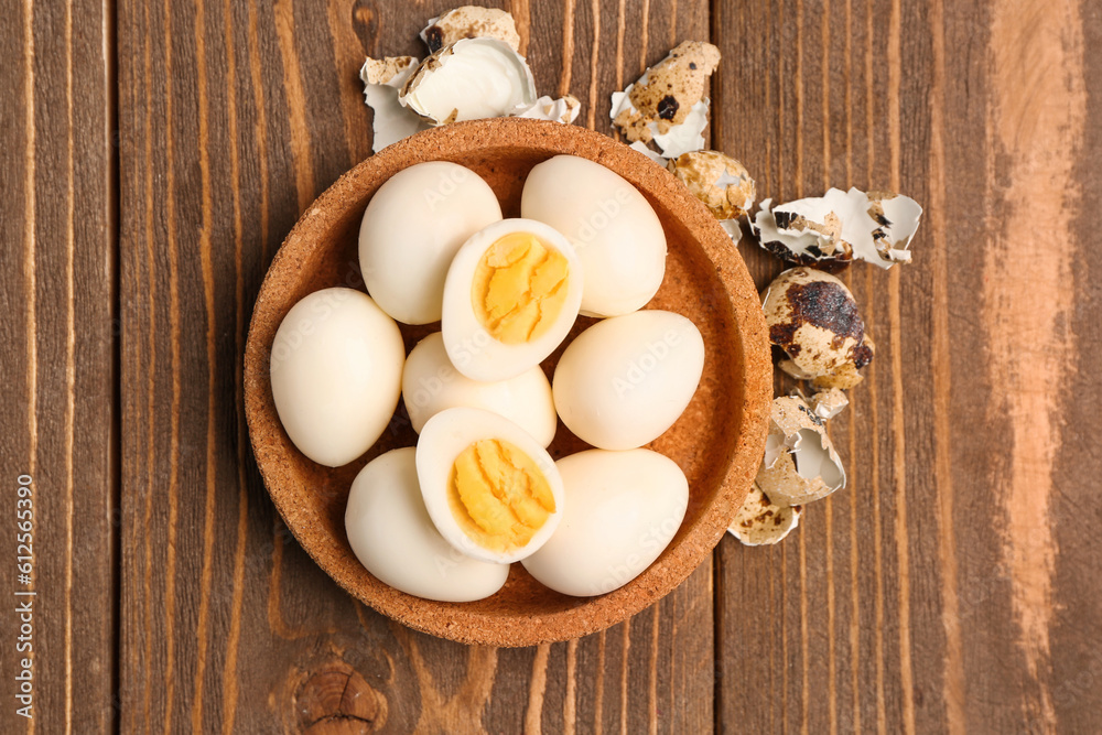 Bowl of boiled quail eggs with shells on wooden background