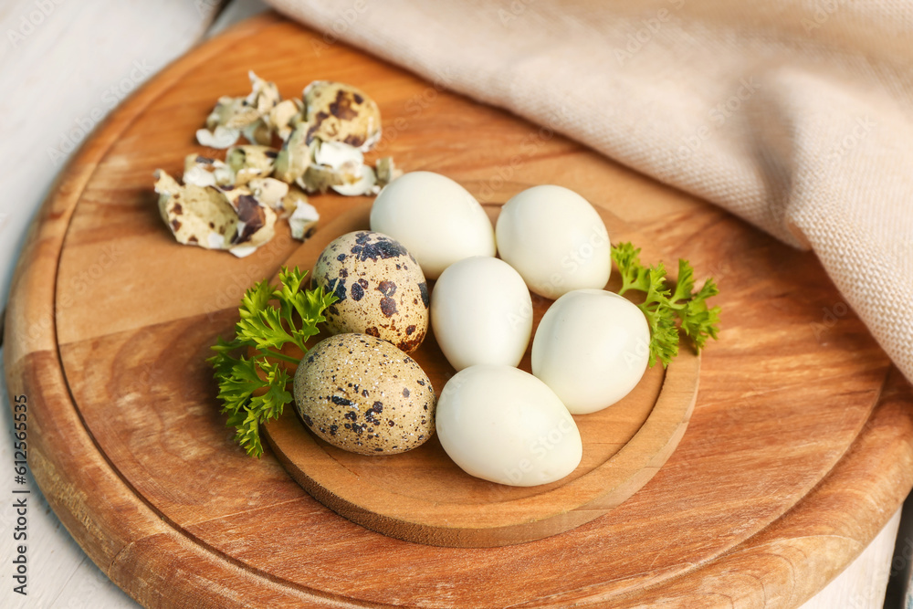 Board of boiled quail eggs with shells on white wooden background