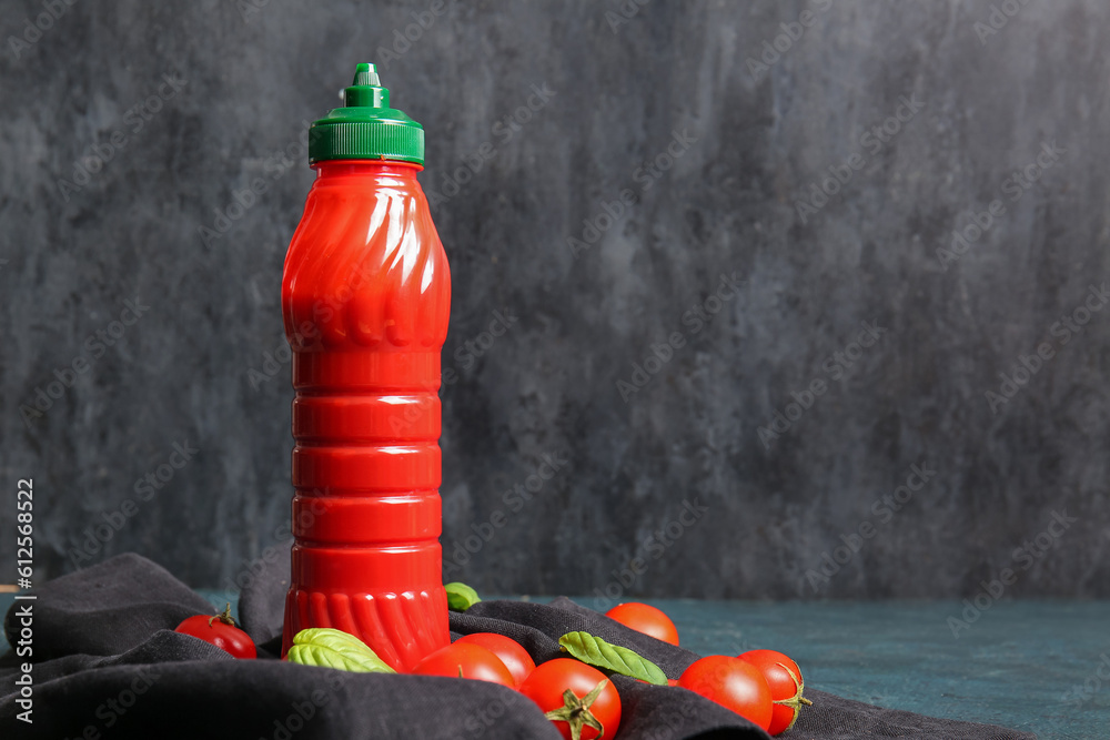 Bottle of ketchup and tomatoes on dark background