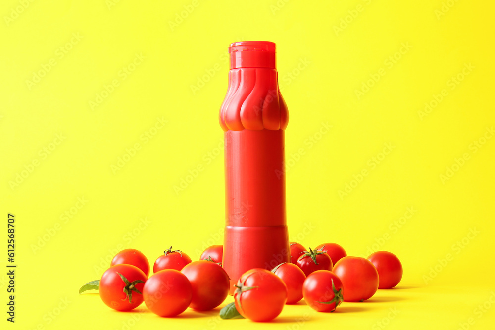 Bottle of ketchup and tomatoes on yellow background