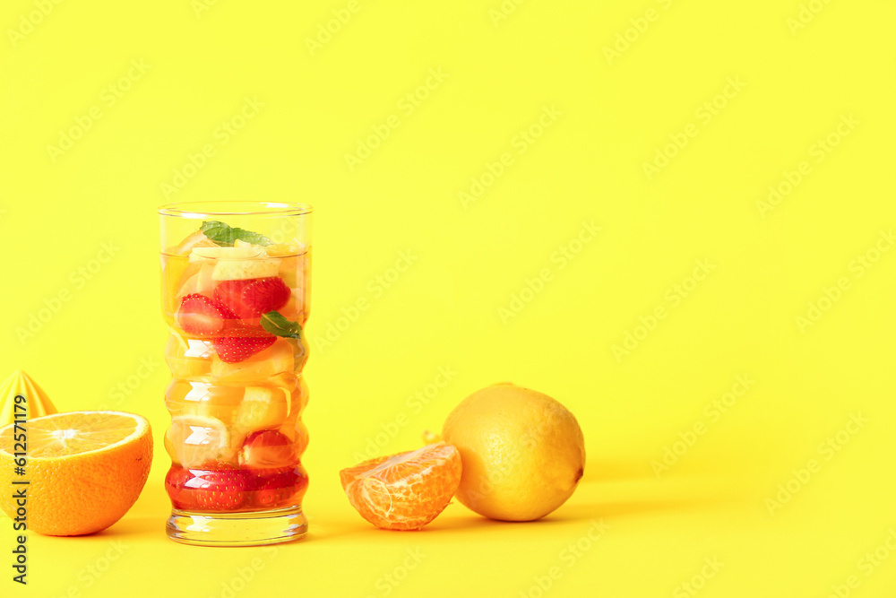 Glass of infused water with different sliced fruits on yellow background