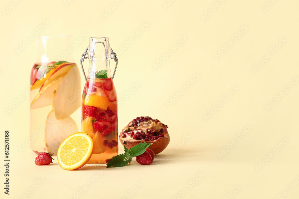 Bottles of infused water with different sliced fruits on beige background