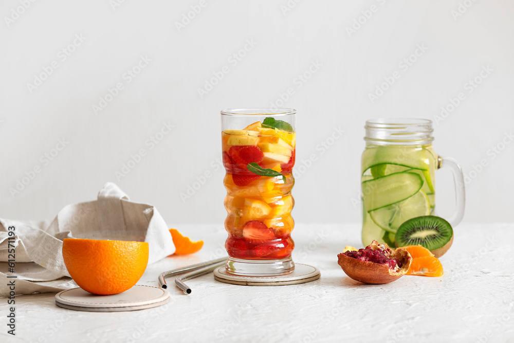 Glass and mason jar of infused water with different sliced fruits on white table