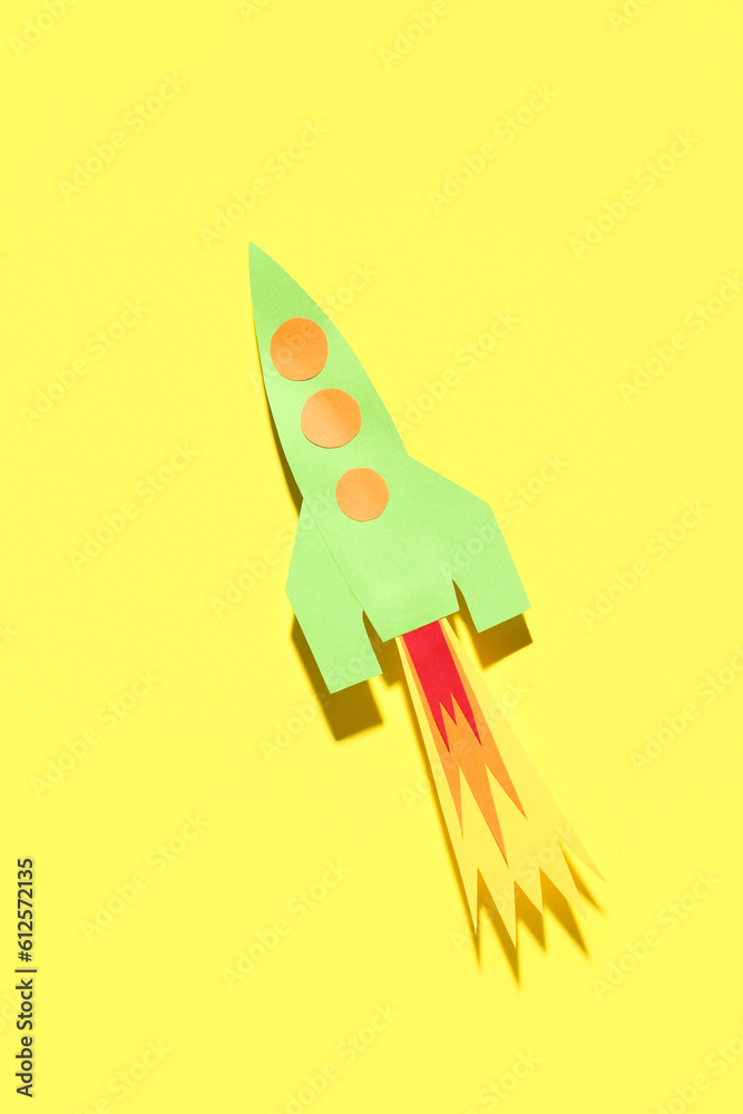 Green paper rocket on yellow background