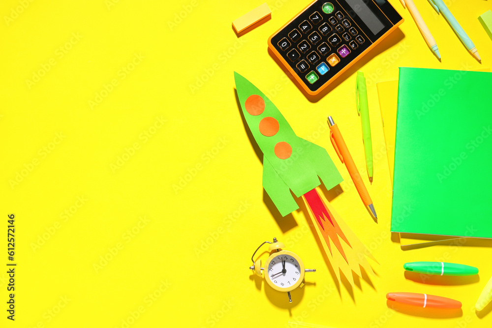 Paper rocket with calculator, alarm clock and different stationery on yellow background