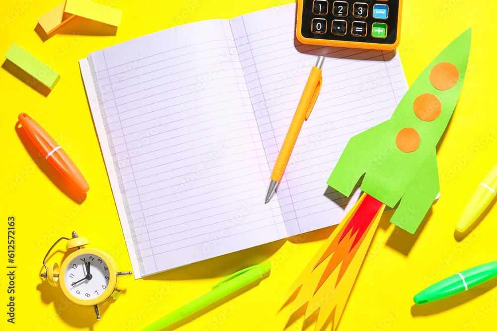 Paper rocket with calculator, blank notebook and different stationery on yellow background