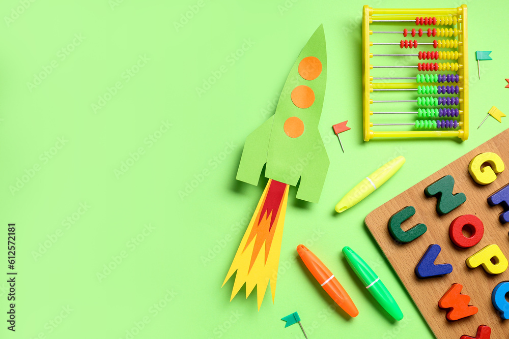 Paper rocket with abacus, wooden letters and stationery on green background