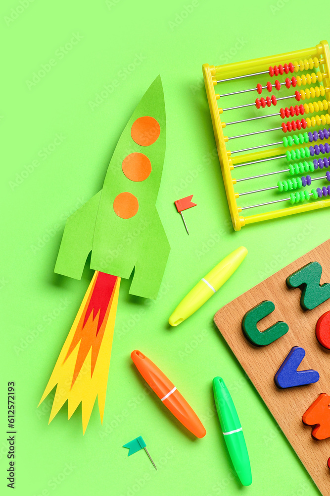 Paper rocket with abacus, wooden letters and stationery on green background