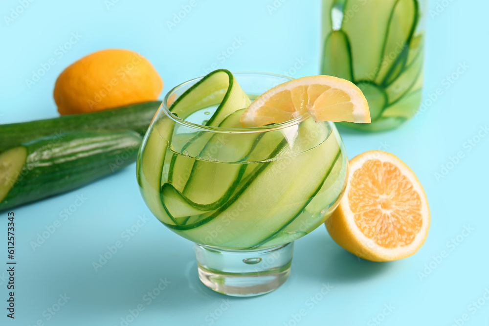 Glass and bottle of infused water with cucumber slices on blue background