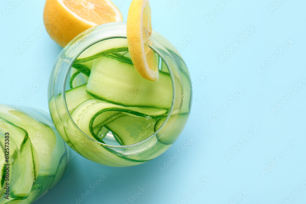 Glass and bottle of infused water with cucumber slices on blue background