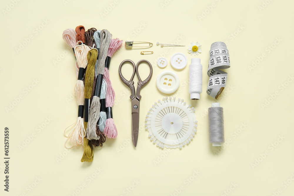 Set of different embroidery supplies on pale yellow background