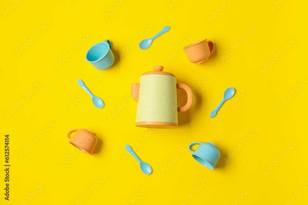 Teapot with frame made of different cups and spoons for baby on yellow background