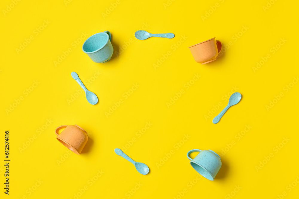 Frame made of different cups and spoons for baby on yellow background