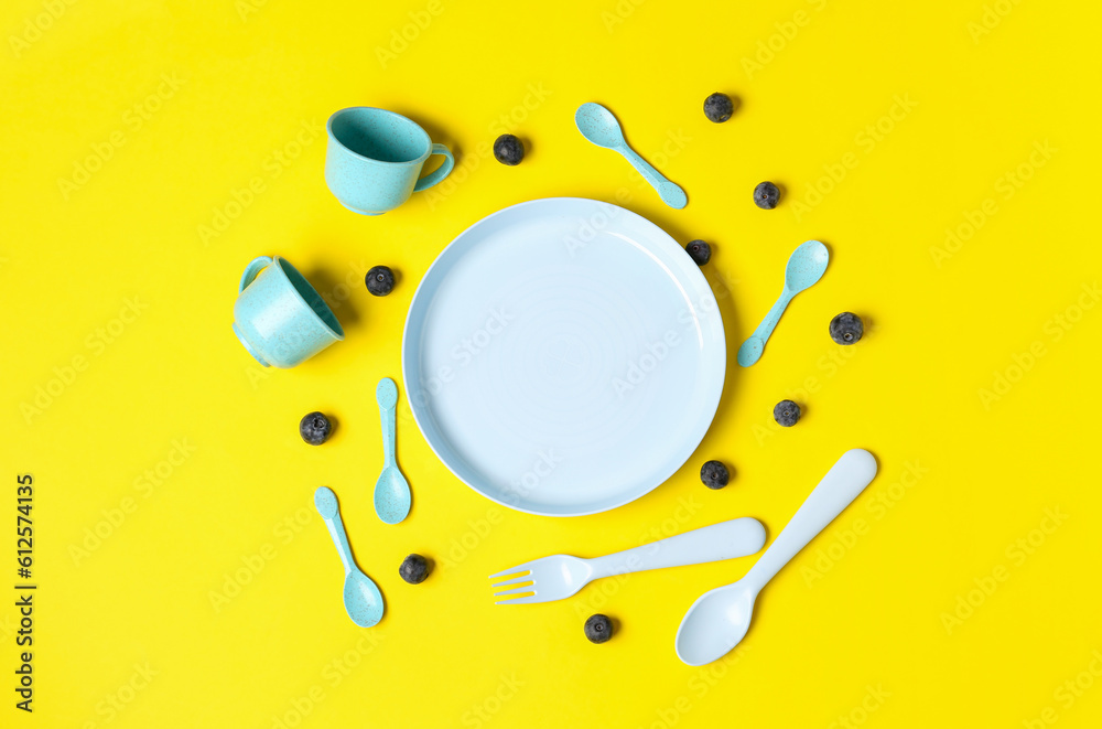 Different eating utensils for baby on yellow background