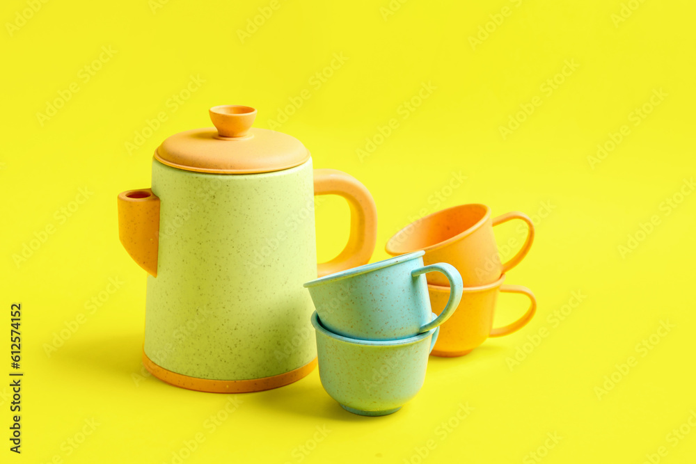 Teapot with cups for baby on yellow background