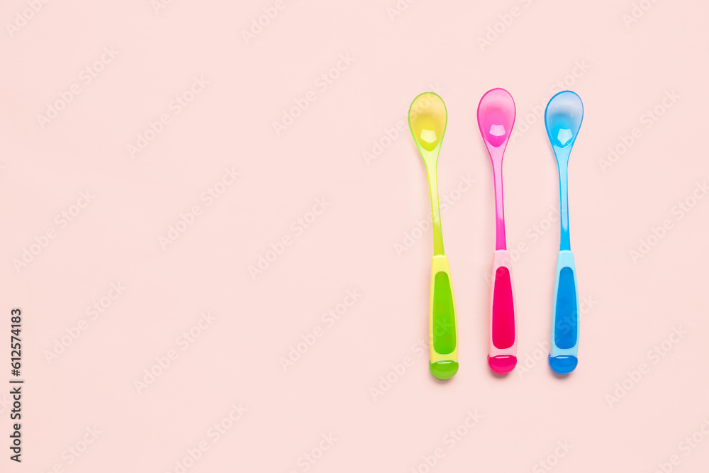 Different colorful spoons for baby on pink background