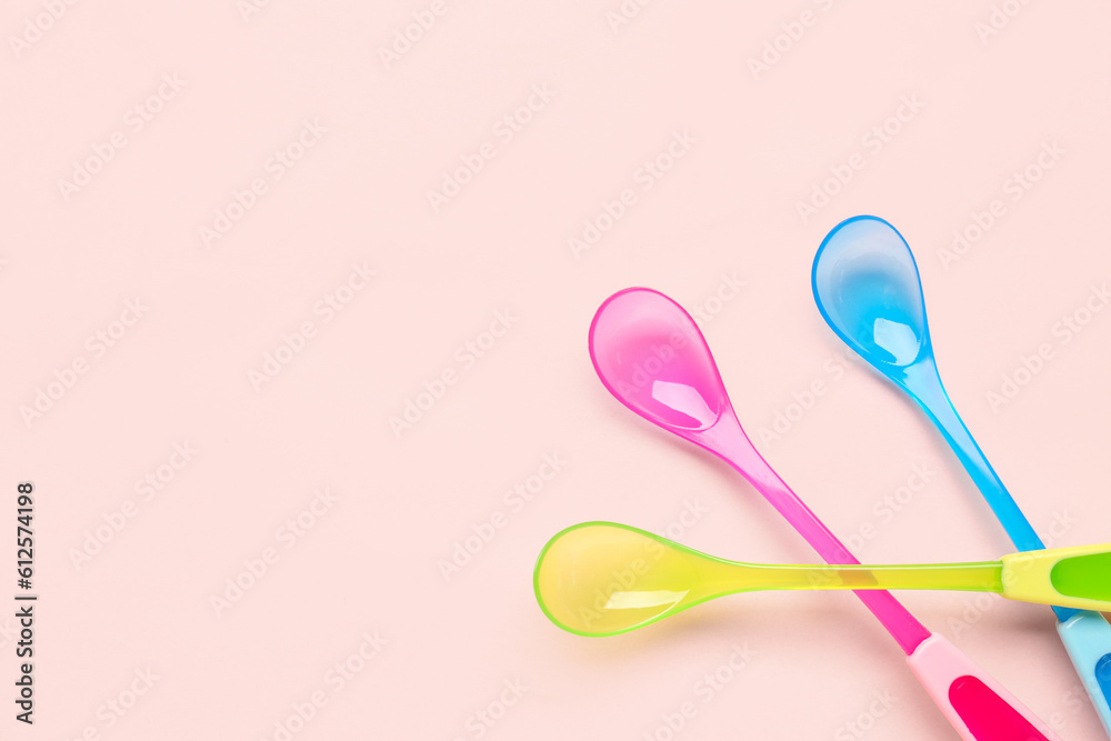 Different colorful spoons for baby on pink background