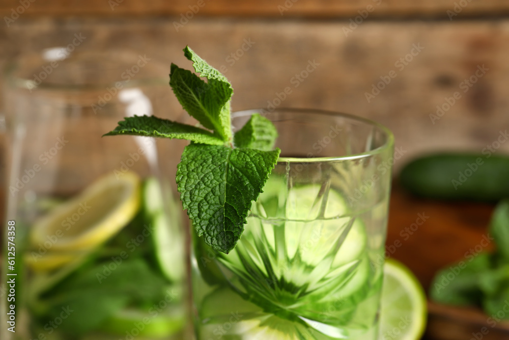 Glass and jug of infused water with cucumber slices on wooden background