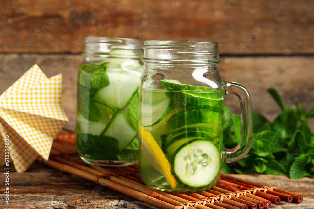 Mason jars of infused water with cucumber slices on wooden background