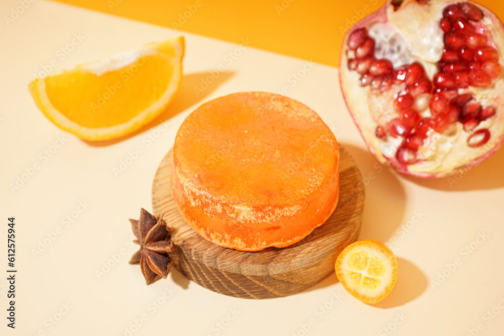 Wooden stand with solid shampoo bar with orange, kumquat and pomegranate on table near orange wall