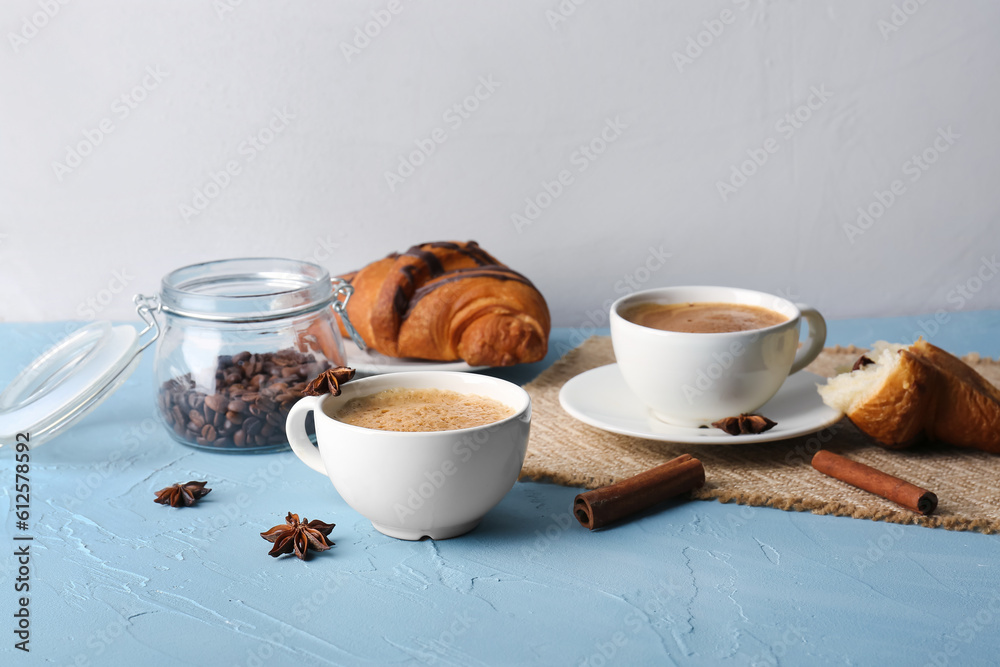 Cups of delicious espresso with coffee beans and croissant on blue background