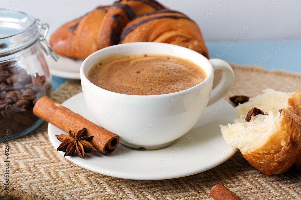 Cup of delicious espresso with coffee beans and croissant on table, closeup