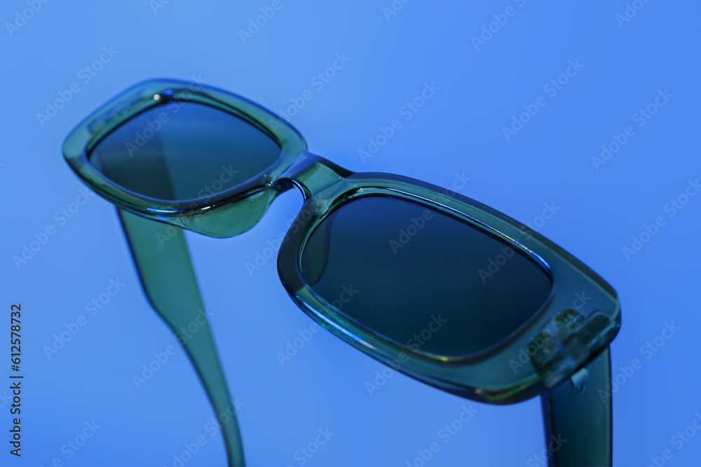 Stylish sunglasses on blue background, closeup