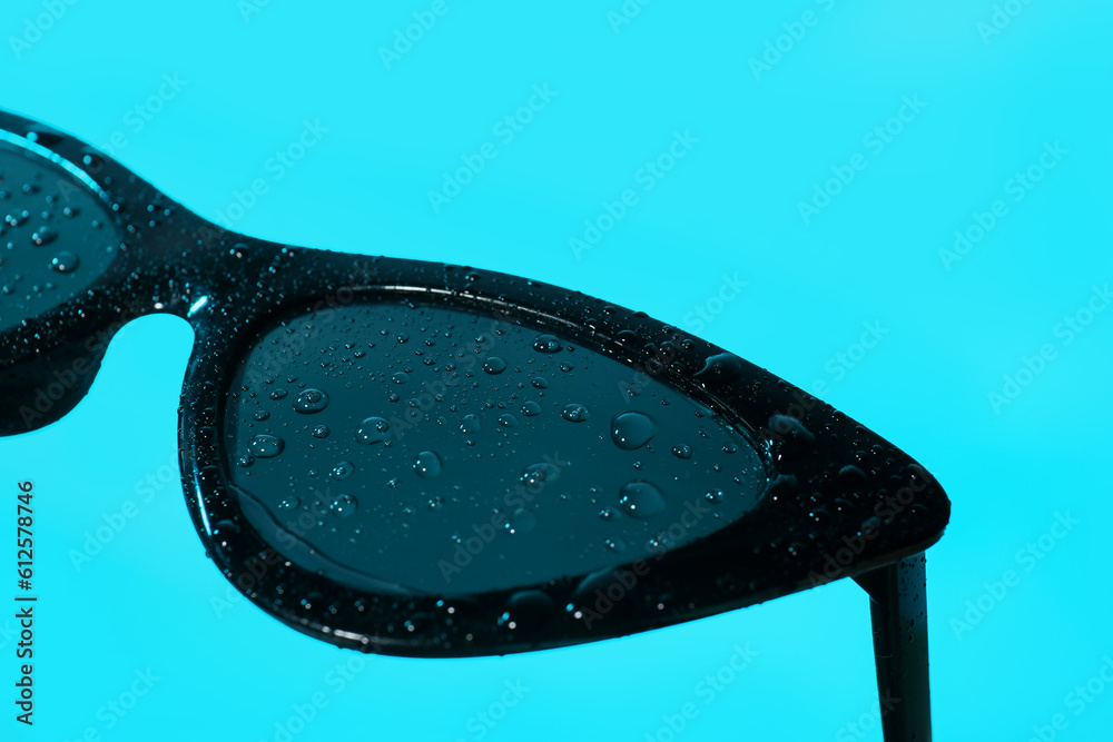 Stylish black sunglasses on turquoise background, closeup