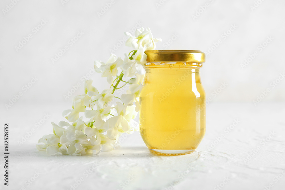 Jar of honey with flowers of acacia on light background, closeup