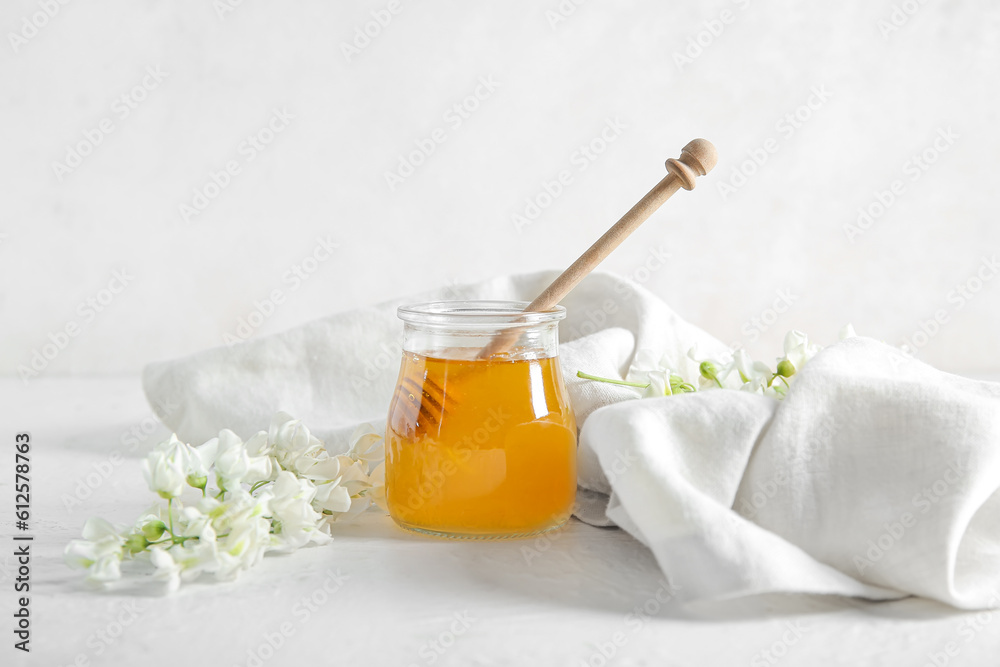 Jar of honey with flowers of acacia and dipper on light background