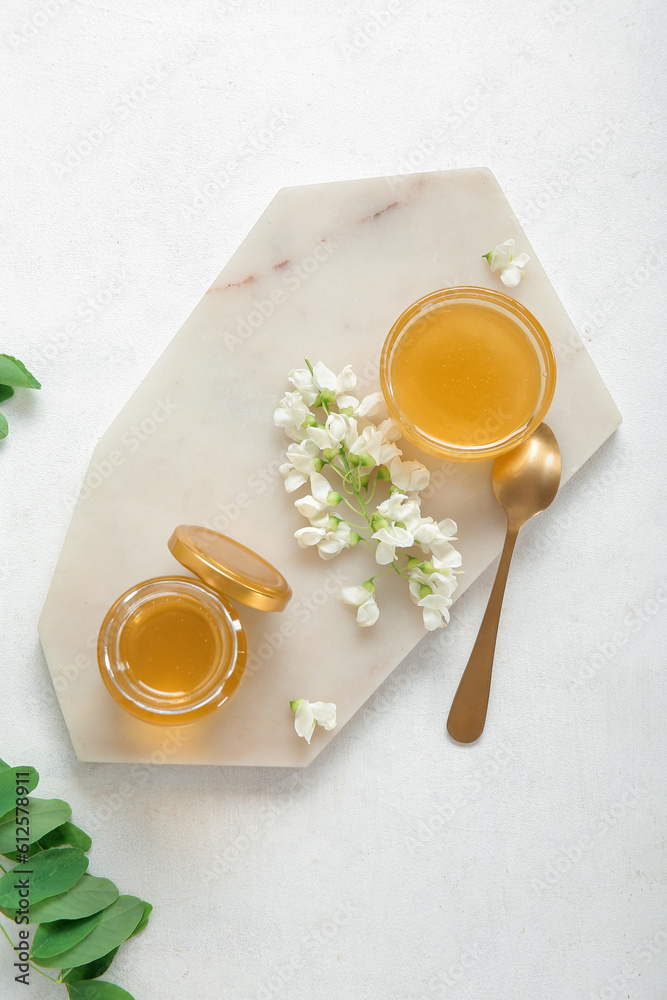 Bowl and jar of honey with flowers of acacia on light background