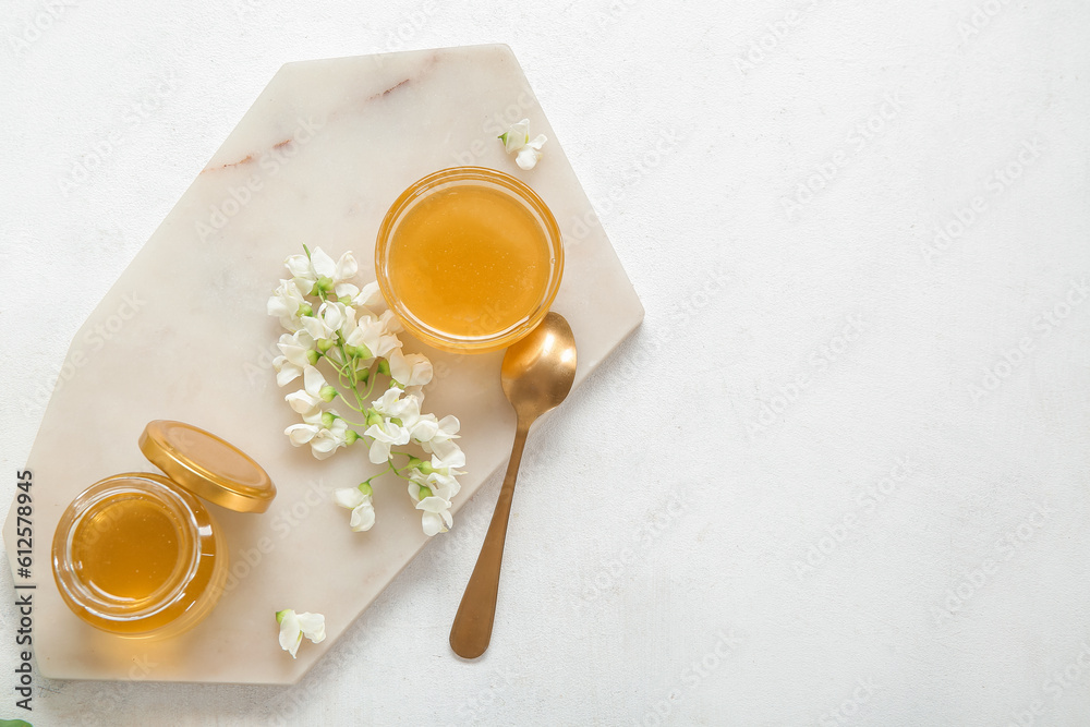 Bowl and jar of honey with flowers of acacia on light background