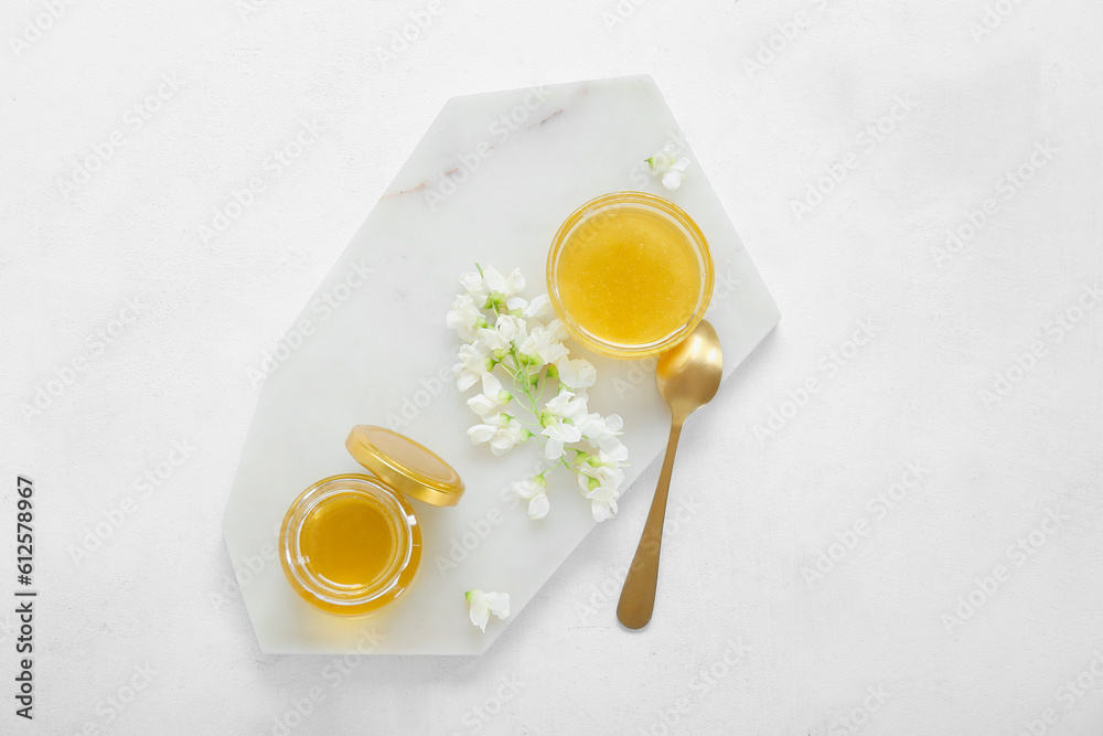 Bowl and jar of honey with flowers of acacia on light background