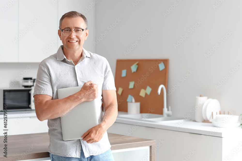 Mature man with eyeglasses and laptop in kitchen