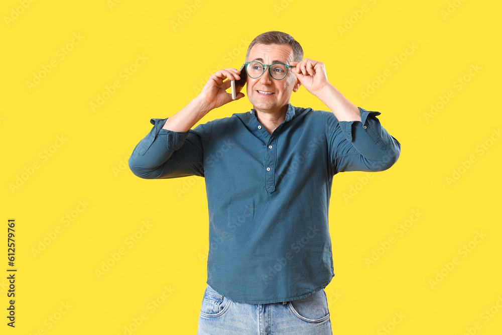 Mature man in eyeglasses talking by mobile phone on yellow background