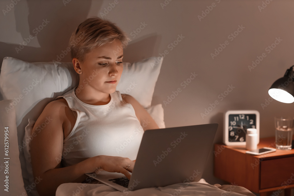 Young woman using laptop in bed at night